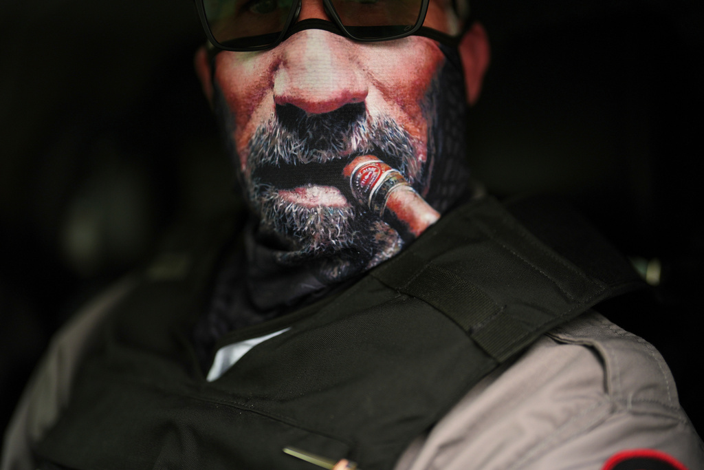 An immigration official wears a face mask depicting a cigar and beard as he waits to transport detained immigrants, July 23, 2025, in Baldwin Park, Calif. (AP Photo/Gregory Bull, File)