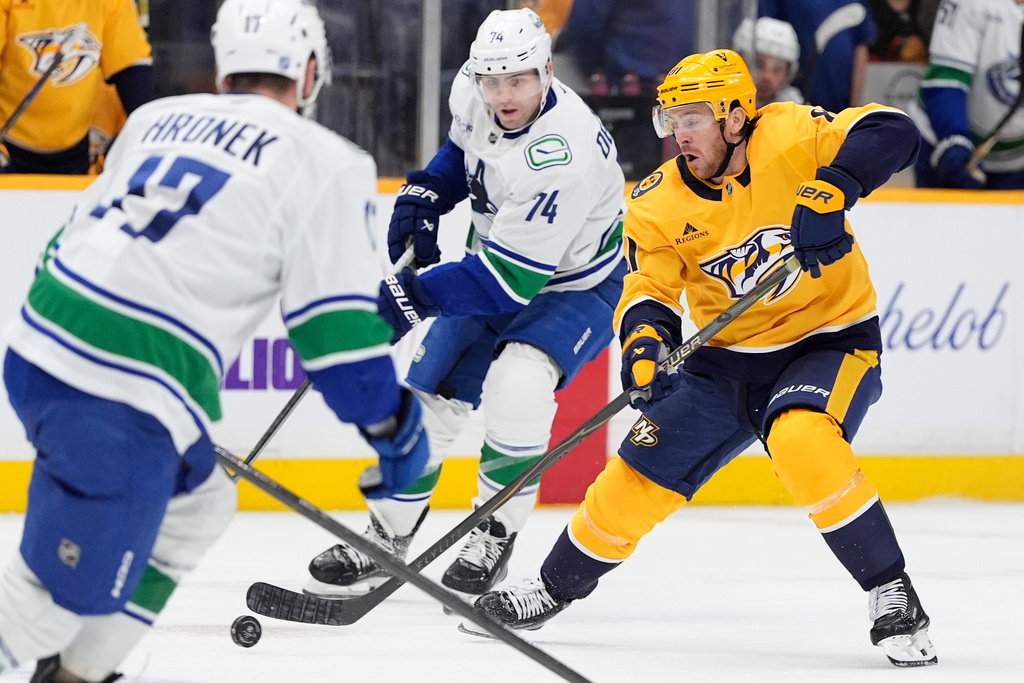 Nashville Predators center Jonathan Marchessault, right, moves the puck past Vancouver Canucks left wing Jake Debrusk (74) and defenseman Filip Hronek (17) during the second period of an NHL hockey game Monday, Nov. 3, 2025, in Nashville, Tenn. (AP Photo/George Walker IV)