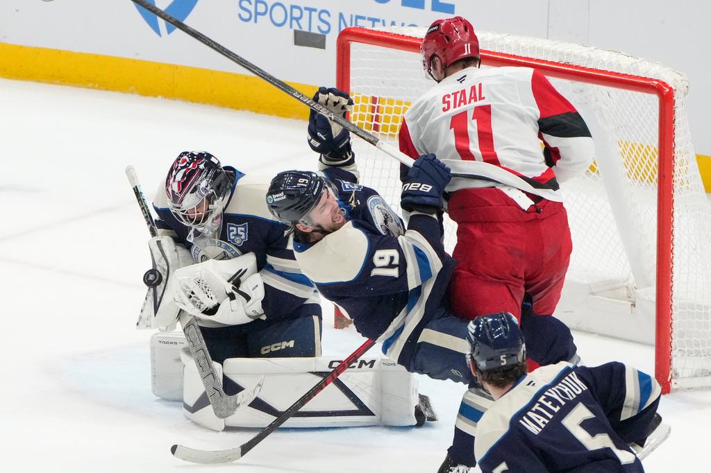 Columbus Blue Jackets goaltender Jet Greaves, left, blocks a shot as Carolina Hurricanes center Jordan Staal (11) checks center Adam Fantilli (19) in the second period of an NHL game in Columbus, Tuesday, March 31, 2026. (AP Photo/Sue Ogrocki)