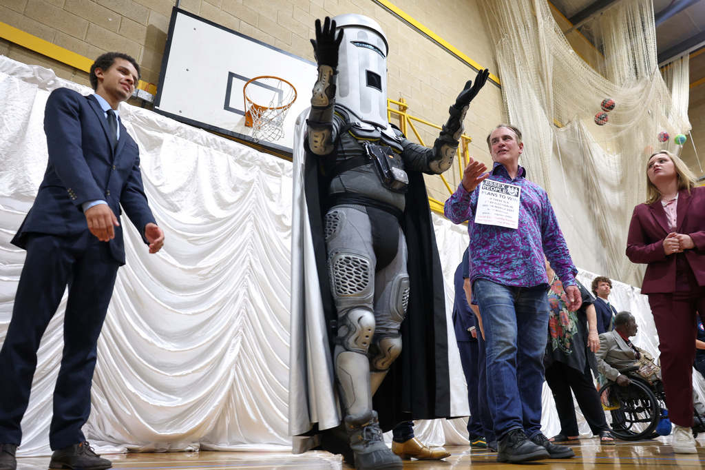 Count Binface, center, stands among other candidates during the result announcement after the Clacton by-election count at the Leisure Centre in Clacton on Sea, England, Friday, Aug. 14, 2026.(AP Photo/Richard Pelham)