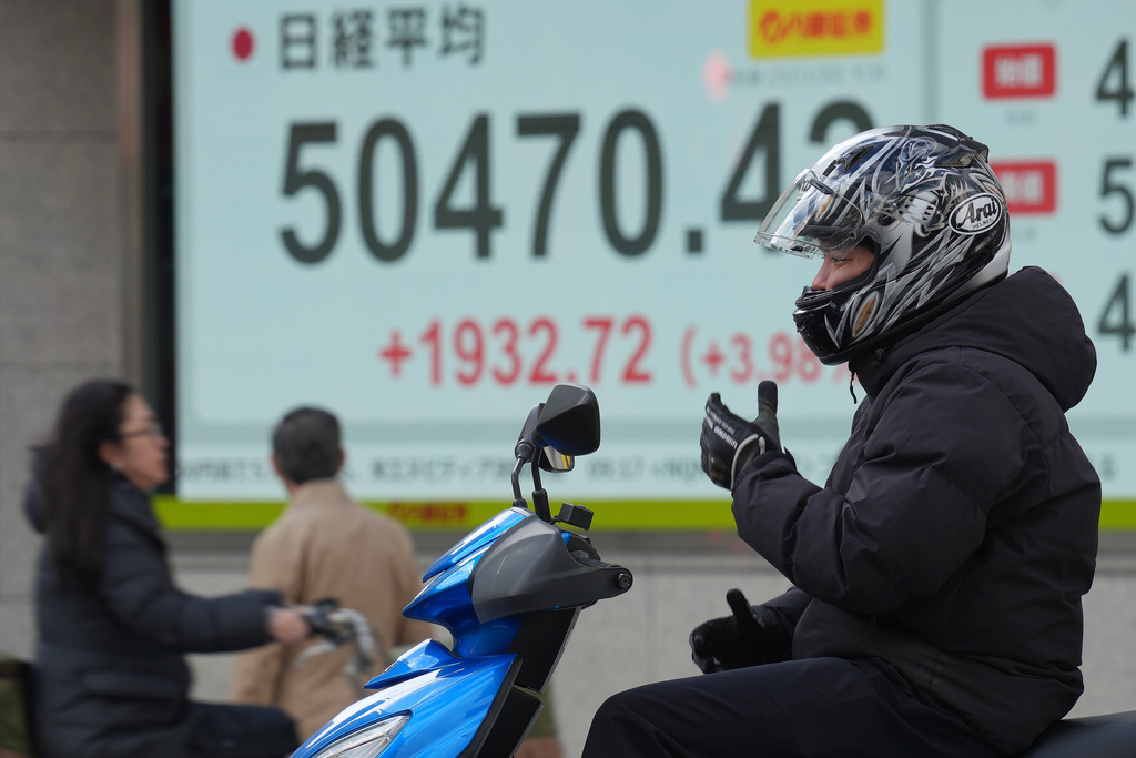 A person rides a scooter in front of an electronic stock board showing Japan's Nikkei index at a securities firm Thursday, Nov. 20, 2025, in Tokyo. (AP Photo/Eugene Hoshiko)