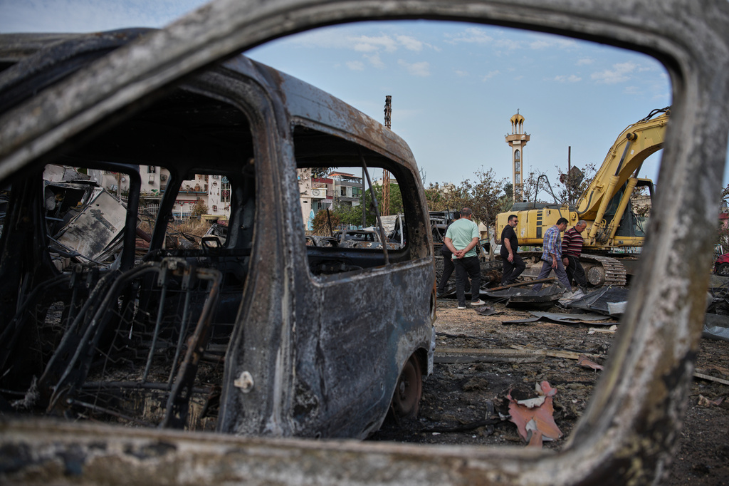 Locals residents walk among vehicles burned in an Israeli airstrike in Jibchit, southern Lebanon, Friday, April 17, 2026, following a ceasefire between Israel and Hezbollah. (AP Photo/Hassan Ammar)