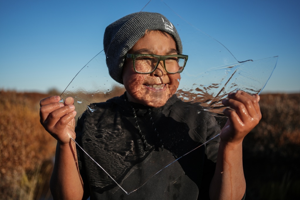 Charles Gallahorn, 10, plays with a slab of ice taken from a pond that formed on a warped road caused by thawing permafrost in Kotzebue, Alaska, Friday, Sept. 26, 2025. (AP Photo/Annika Hammerschlag)