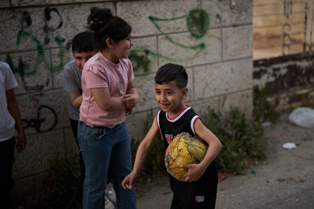 A Palestinian boy carries a worn soccer ball while playing with friends in an alley in the West Bank town of Al-Ram, Monday, May 11, 2026. (AP Photo/Leo Correa)