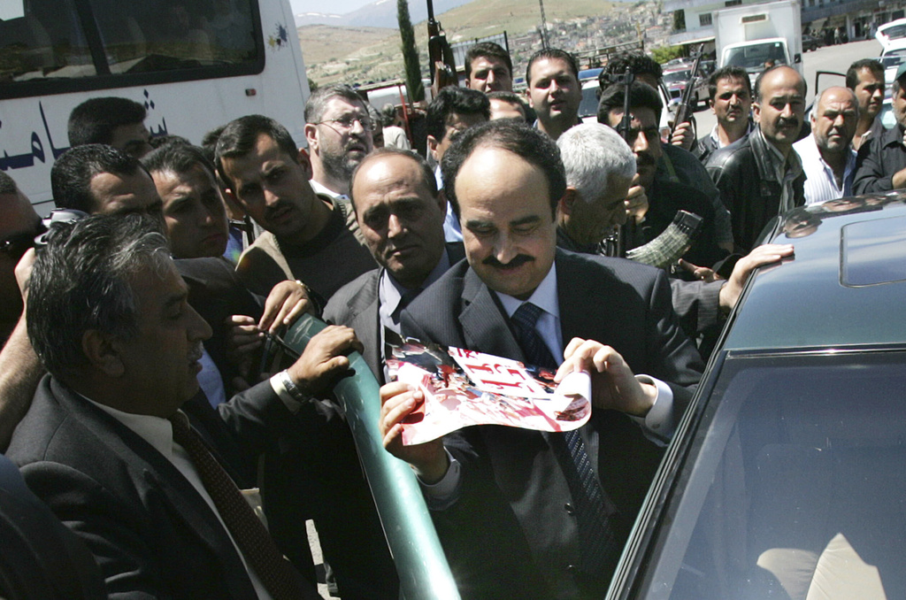 FILE - Then former head of the Syrian political security branch Maj. Gen. Rostom Ghazali, center, who also was a former Syrian intelligence chief in Lebanon, escorted by his supporters as he looks to an Arabic placard that reads:"Thanks Syria," after he get out from his car on his way cross the Lebanese border point of Masnaa in the Bekaa Valley, east of Beirut, Lebanon, April 26, 2005. (AP Photo/Hussein Malla, File)