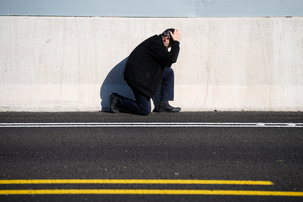 A man takes cover by the side of the road as an air raid sirens warn of incoming Iranian missile strikes in Tel Aviv, Israel, March 17, 2026. (AP Photo/Ohad Zwigenberg)