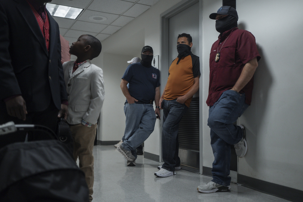 Federal agents watch as a family of asylum seekers from Haiti prepares to enter an immigration courtroom, Tuesday, Aug. 26, 2025, in New York. (AP Photo/Olga Fedorova)