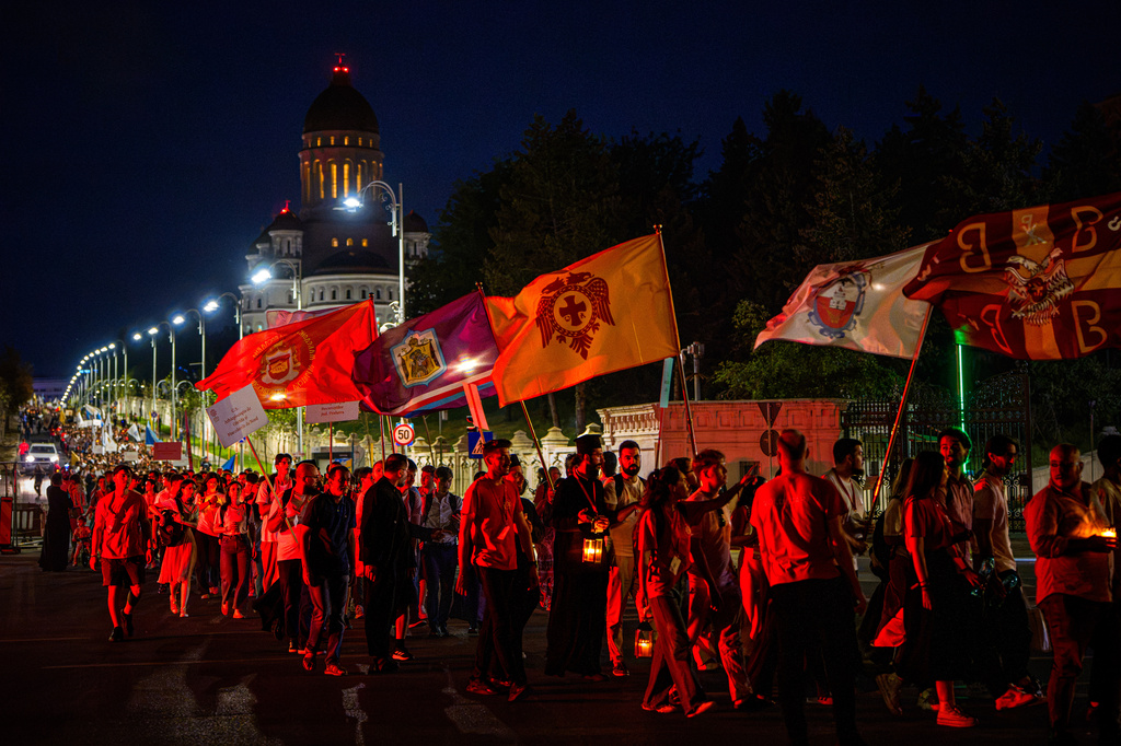 People wave flags backdropped by the National Cathedral during the Procession of Lights, part of a four-day program of the International Meeting of Orthodox Youth (ITO), in Bucharest, Romania, Wednesday, Sept. 2, 2026. (AP Photo/Andreea Alexandru)