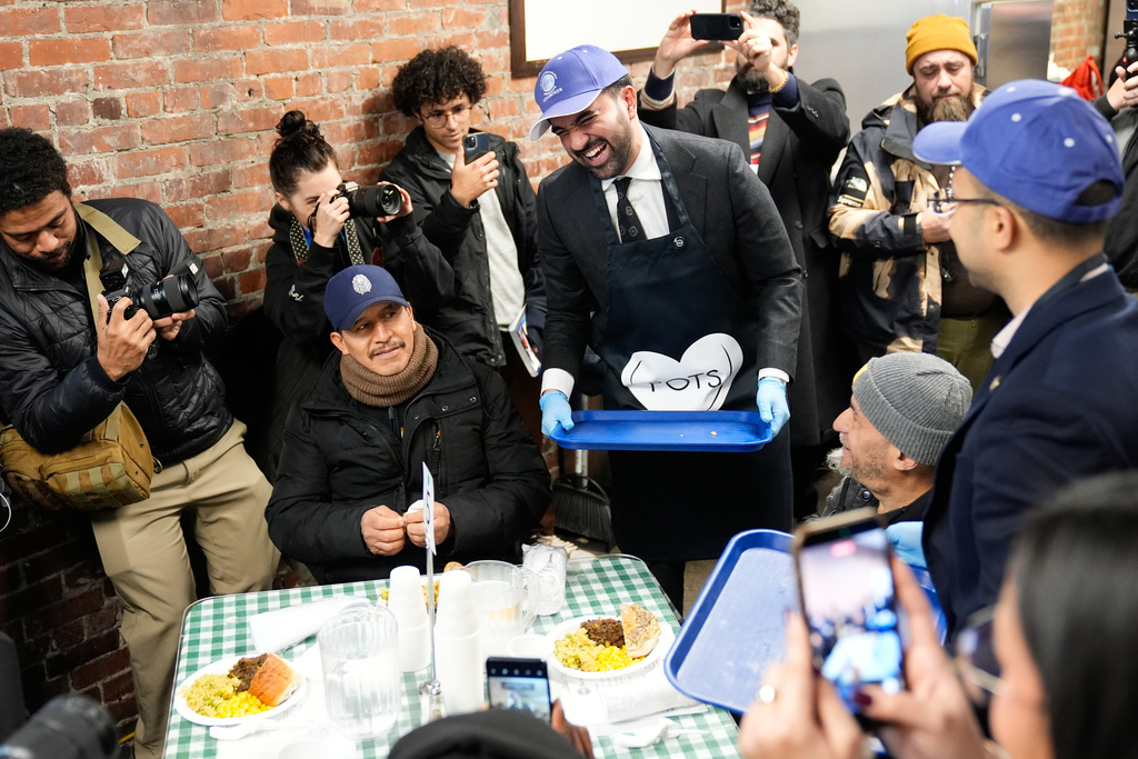 While surrounded by members of the media, New York City mayor-elect Zohran Mamdani, center, helps to serve meals at at POTS, a Bronx nonprofit that provides food assistance, in New York, Monday, Nov. 17, 2025. (AP Photo/Seth Wenig)