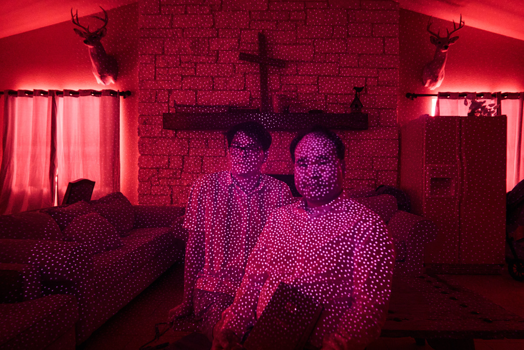 Pastor Pan Yongguang, right, and his son Paul, members of a Chinese church living in exile after fleeing from China, are illuminated by cellphone infrared facial recognition beams while sitting for a photo in the community room of the ranch compound where they're living in Midland, Texas, Oct. 11, 2025. (AP Photo/David Goldman)