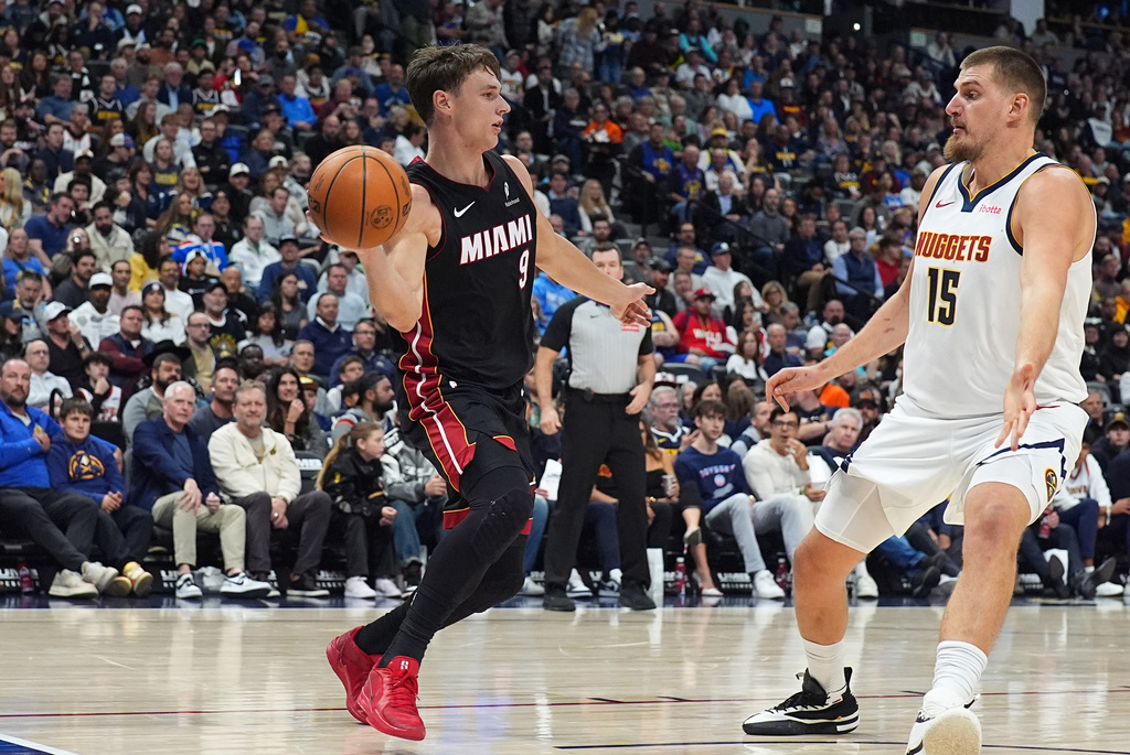 Miami Heat guard Pelle Larsson, left, passes the ball as Denver Nuggets center Nikola Jokic defends in the first half of an NBA basketball game Wednesday, Nov. 5, 2025, in Denver. (AP Photo/David Zalubowski)
