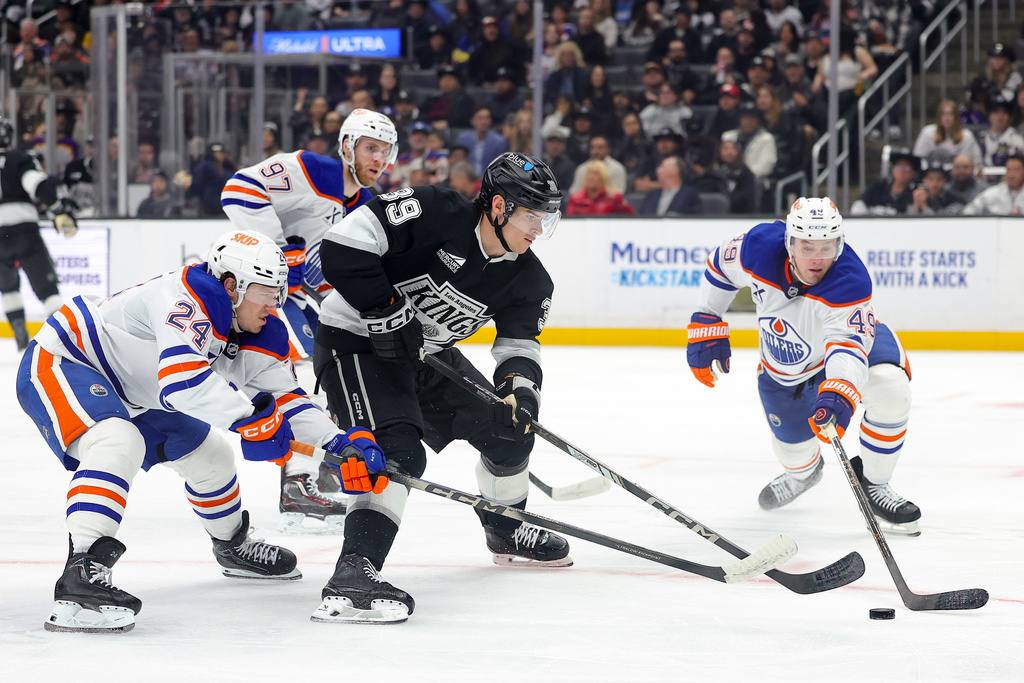 Los Angeles Kings left wing Jeff Malott, third from left, moves the puck against Edmonton Oilers defenseman Spencer Stastney, center Connor McDavid, and defenseman Ty Emberson, from left, during the second period of an NHL hockey game Thursday, Feb. 26, 2026 in Los Angeles. (AP Photo/Ryan Sun)
