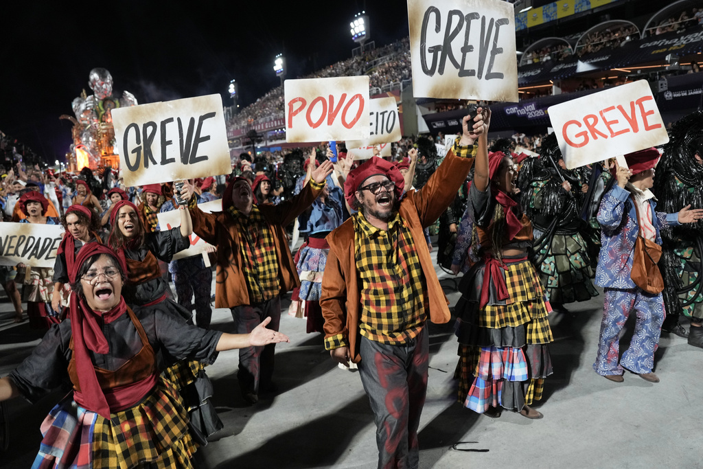 Performers of Academicos de Niteroi samba school, hold signs that read "Strike" and "People" during Carnival celebrations at the Sambadrome in Rio de Janeiro, Sunday, Feb. 15, 2026. (AP Photo/Silvia Izquierdo)