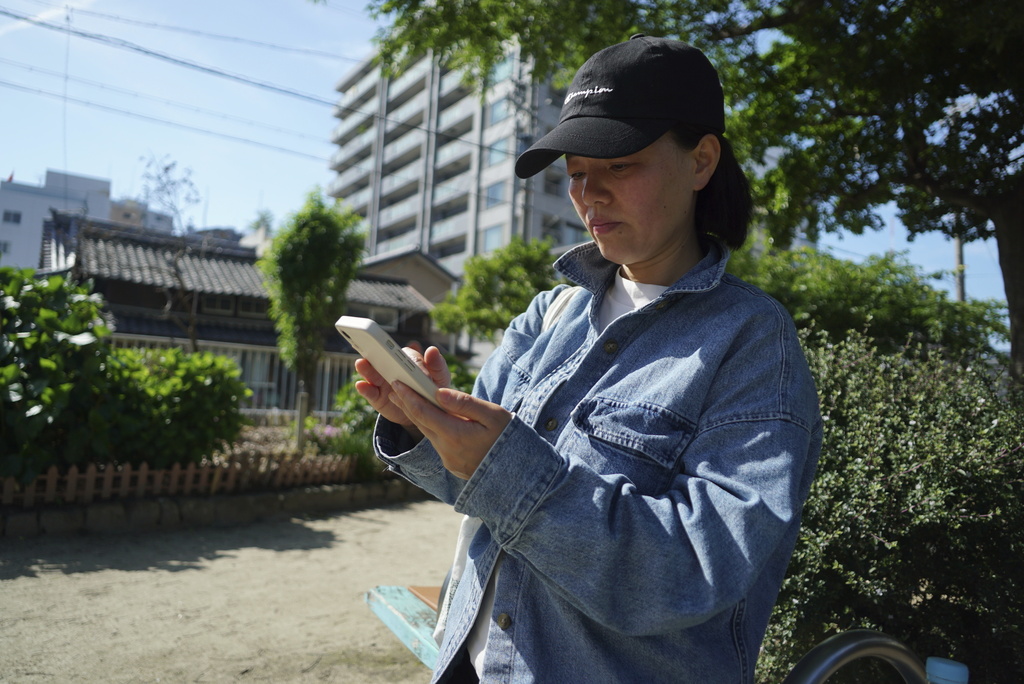 Yang Caiying, who is living in exile in Japan, scrolls through her phone in Nagoya, Japan, Friday, May 17, 2024. (AP Photo/Dake Kang)