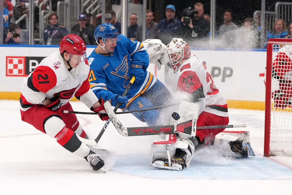 Carolina Hurricanes goaltender Brandon Bussi (32) deflects a puck as teammate Carolina Hurricanes' Alexander Nikishin, left, and St. Louis Blues' Jimmy Snuggerud, center, watch during the second period of an NHL hockey game Tuesday, Jan. 13, 2026, in St. Louis. (AP Photo/Jeff Roberson)