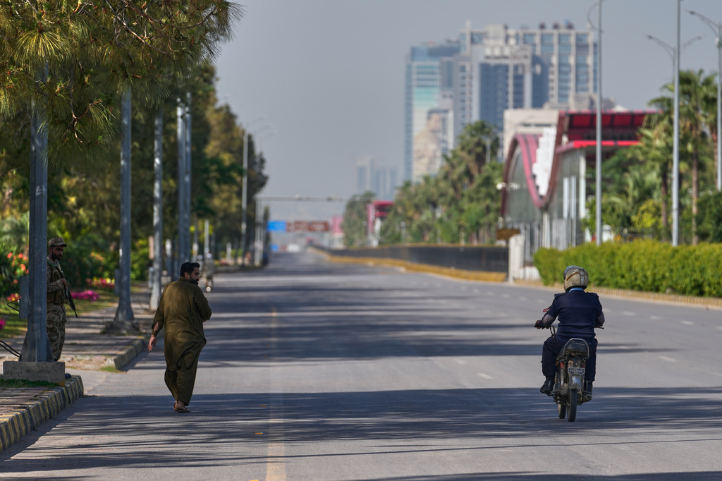An army soldier, left, walks as police officer drives motorcycle on an empty road ahead of second round of negotiations between the U.S. and Iran, in Islamabad, Pakistan, Monday, April 20, 2026. (AP Photo/Anjum Naveed)