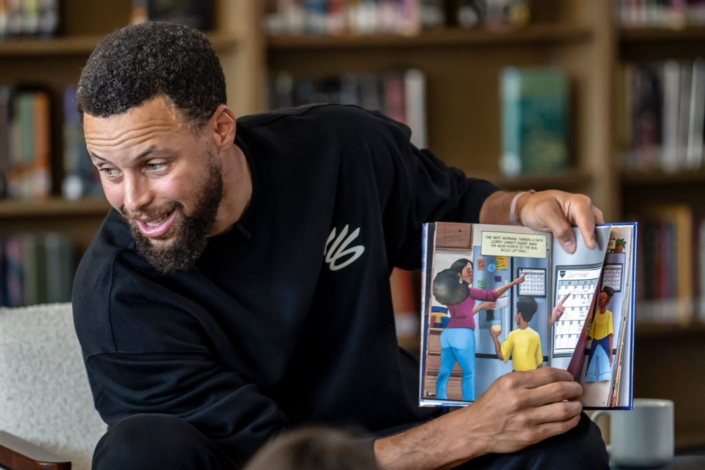 Warriors star Stephen Curry reads from the book, "Eye on the Ball" with students in the library during an event for his Eat.Learn.Play. Foundation at Madison Park Academy Primary in Oakland, Calif., on Wednesday, Sept. 23, 2026. (Carlos Avila Gonzalez/San Francisco Chronicle via AP)