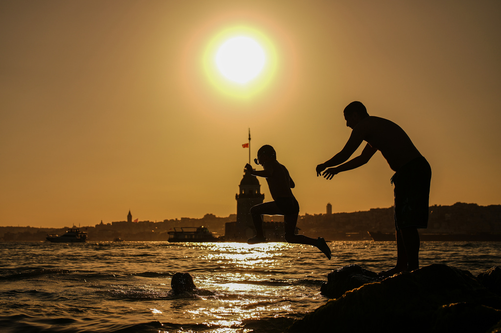 People jump into the Bosphorus with the Maiden's Tower in the background during sunset in Istanbul, Turkey, Sunday, June 28, 2026.(AP Photo/Emrah Gurel)