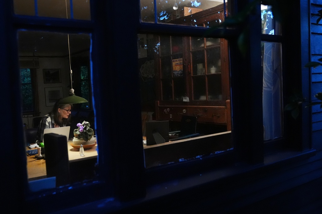 Seeing through the window, Mary E. Brunkow is seen answering messages and emails after winning a Nobel Prize in medicine for part of her work on peripheral immune tolerance, in Seattle, Monday, Oct. 6, 2025. Next to her is her dog Zelda. (AP Photo/Lindsey Wasson)