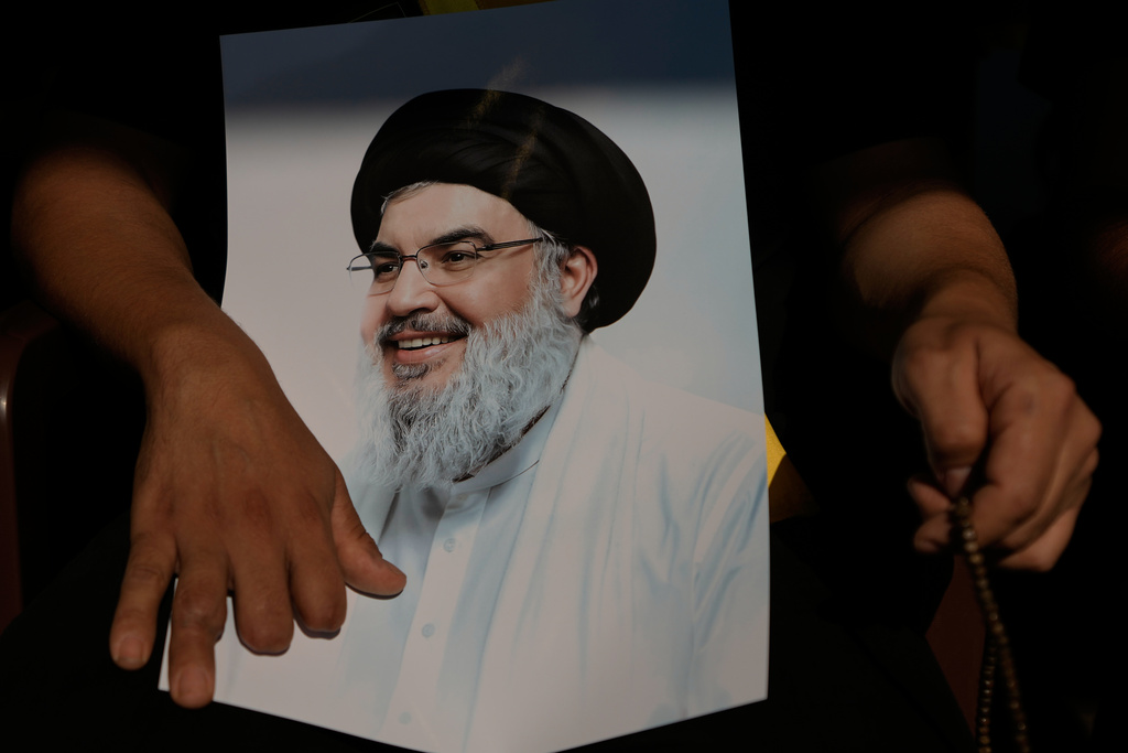 A Hezbollah member who lost several of his fingers during Sept. 17, 2024 pager explosions, holds a picture of Hezbollah leader Sayyed Hassan Nasrallah, who was killed in Israeli airstrikes, marking the first anniversary of Nasrallah's assassination at his grave in Beirut, Lebanon, Saturday, Sept. 27, 2025. (AP Photo/Bilal Hussein)