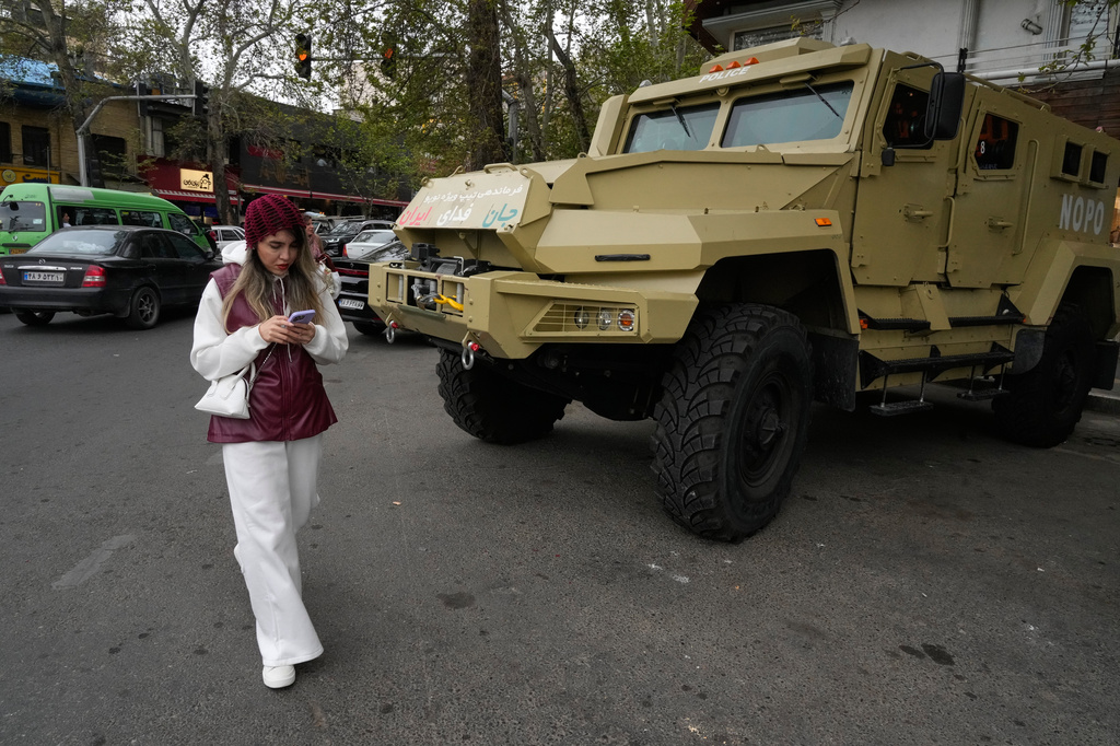 A woman checks her smartphone while walking past a police special forces car at Tajrish Square in northern Tehran, Iran, Sunday, April 12, 2026. (AP Photo/Vahid Salemi)
