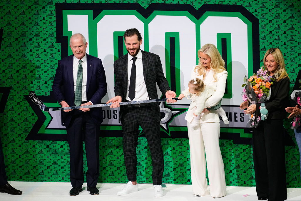 Dallas Stars General Manager is Jim Nill, left, presents Tyler Seguin, center, with a 1000-game trophy stick as he wife Kate, and child look on before an NHL hockey game agianst the Florida Panthers in Dallas, Saturday, Dec. 13, 2025. (AP Photo/Tony Gutierrez)