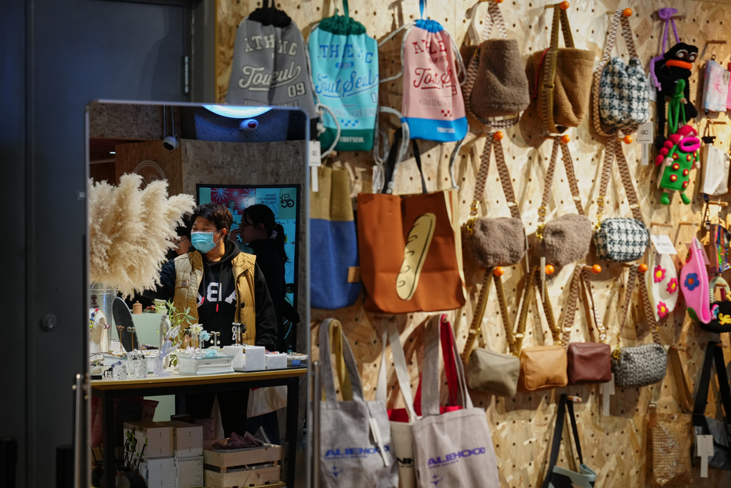 Shoppers are reflected on a mirror of a store selling fashion accessories and bags inside a shopping mall, in Beijing, Sunday, Nov. 30, 2025. (AP Photo/Andy Wong)