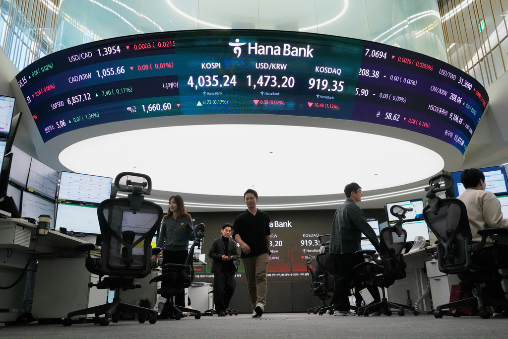 Currency traders pass by a screen showing the Korea Composite Stock Price Index (KOSPI), top center left, and the foreign exchange rate between U.S. dollar and South Korean won, top center, at the foreign exchange dealing room of the Hana Bank headquarters, in Seoul, South Korea, Friday, Dec. 5, 2025. (AP Photo/Ahn Young-joon)