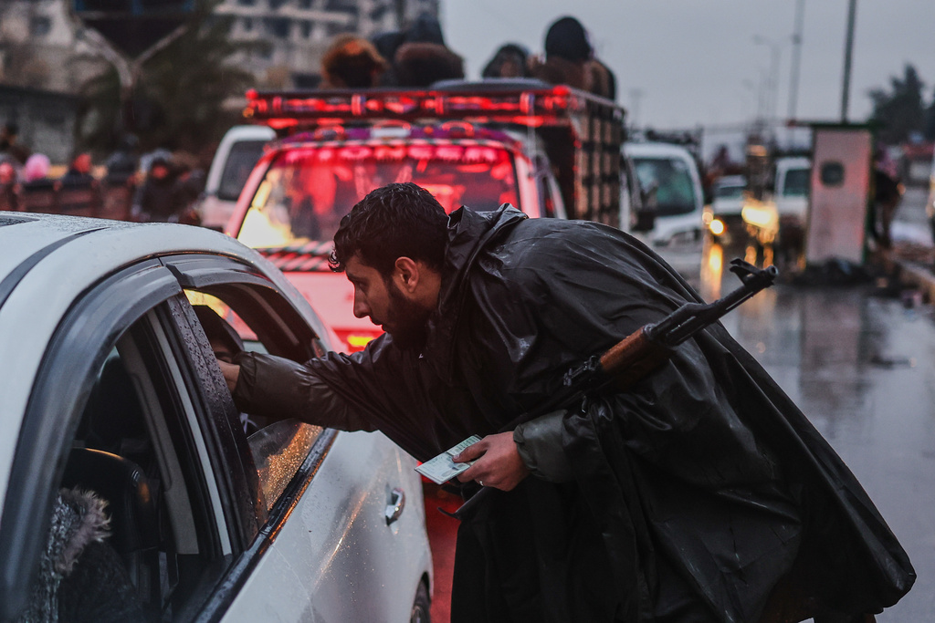 A Syrian forces officer checks the IDs of residents fleeing the Sheikh Maqsoud neighborhood of Aleppo, Syria, Friday, Jan. 9, 2026, after the government declared the area a closed military zone following days of clashes between government forces and Kurdish fighters. (AP Photo/Ghaith Alsayed)