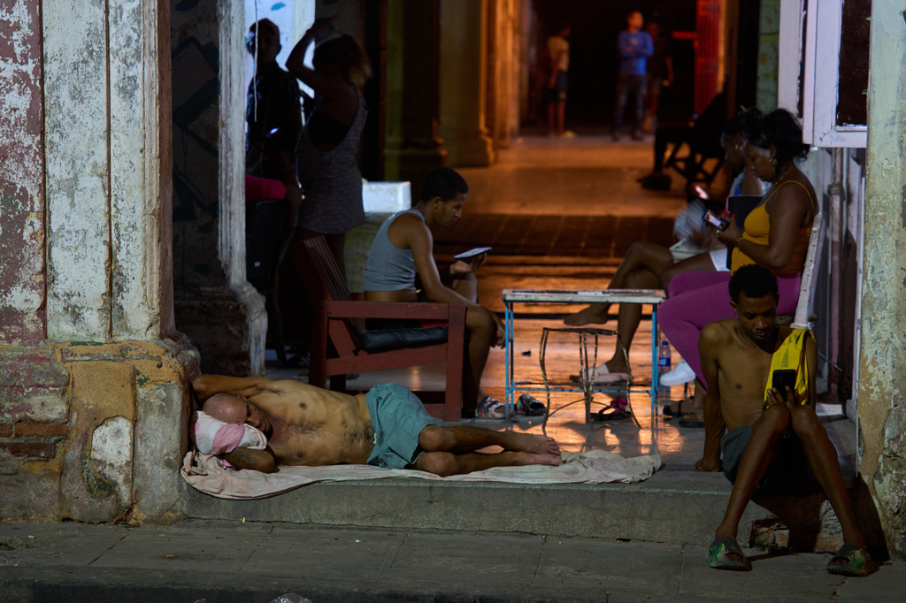 A man sleeps in the doorway of his home while others pass the time trying to cool off in the street in Havana, Cuba, Tuesday, Aug. 4, 2026. (AP Photo/Ramon Espinosa)