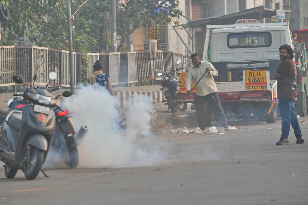A municipal worker sweeps as a person burns firecrackers amidst morning smog in New Delhi, India, Tuesday, Oct. 21, 2025. (AP Photo/Manish Swarup)