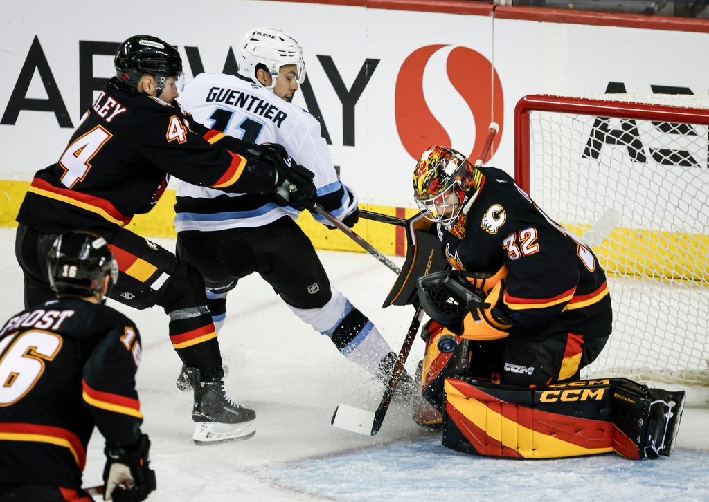 Utah Mammoth's Dylan Guenther, second from right, has his shot blocked by Calgary Flames goalie Dustin Wolf, right, as Flames' Joel Hanley, top left, checks him during third-period NHL hockey game action in Calgary, Alberta, Saturday, Dec. 6, 2025. (Jeff McIntosh/The Canadian Press via AP)