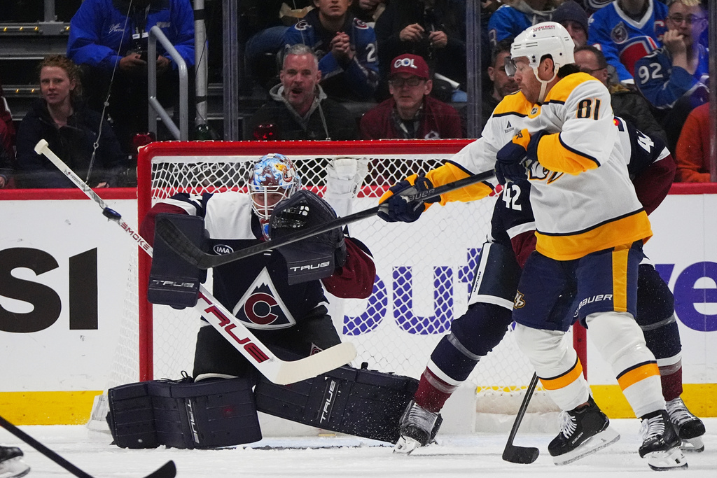 Nashville Predators center Jonathan Marchessault, front right, redirects the puck at Colorado Avalanche goaltender Scott Wedgewood, left, while battling for position with defenseman Josh Manson in the first period of an NHL hockey game Saturday, Dec. 13, 2025, in Denver. (AP Photo/David Zalubowski)