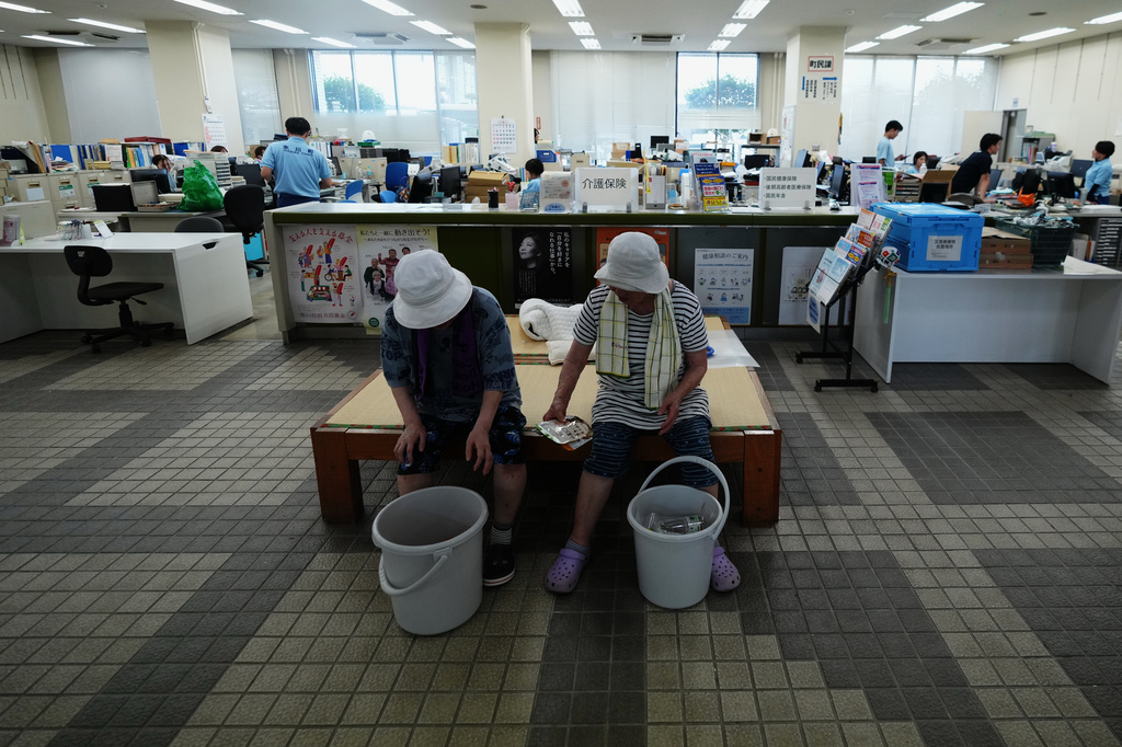 Women rest at the Hikawa Town Hall after receiving food and water supplies distributed outside the building in Hikawa, southern Japan, Thursday, July 30, 2026, two days after an earthquake hit the area. (AP Photo/Hiro Komae)