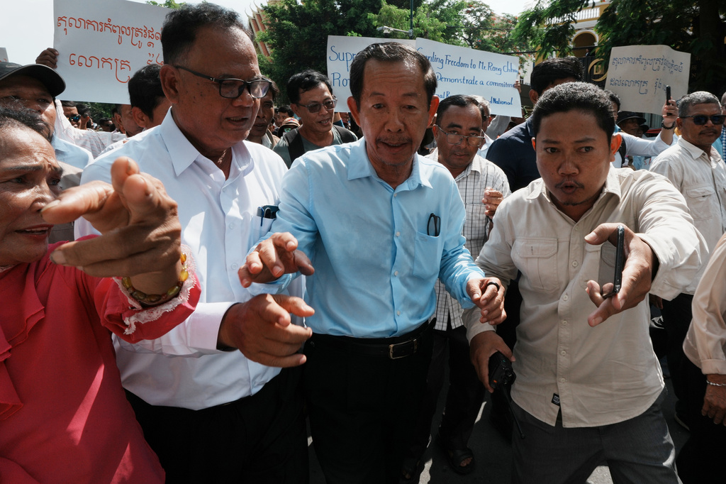 A security guard in civil uniform, right, guides Rong Chhun, a prominent Cambodian opposition politician, center, as he leaves a Supreme Court hearing in Phnom Penh, Cambodia, Monday, June 15, 2026. (AP Photo/Heng Sinith)
