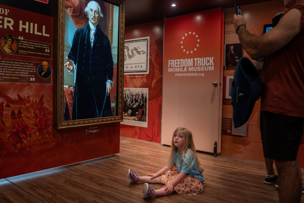 A child sits in front of a video of George Washington at the Great American State Fair on the National Mall, Friday, July 3, 2026, in Washington. (AP Photo/Nathan Howard)