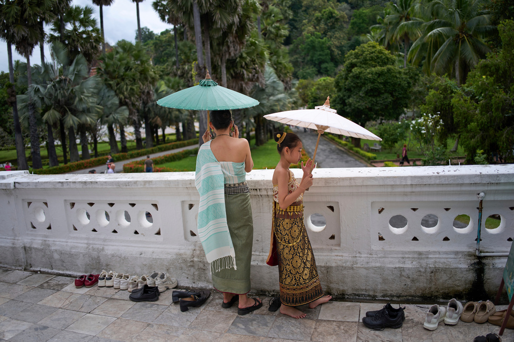A woman and a young girl wearing traditional formal Lao dress stand barefoot as they hold parasols on a temple terrace in Luang Prabang, Laos, Sunday, Nov. 2, 2025. (AP Photo/Eugene Hoshiko)