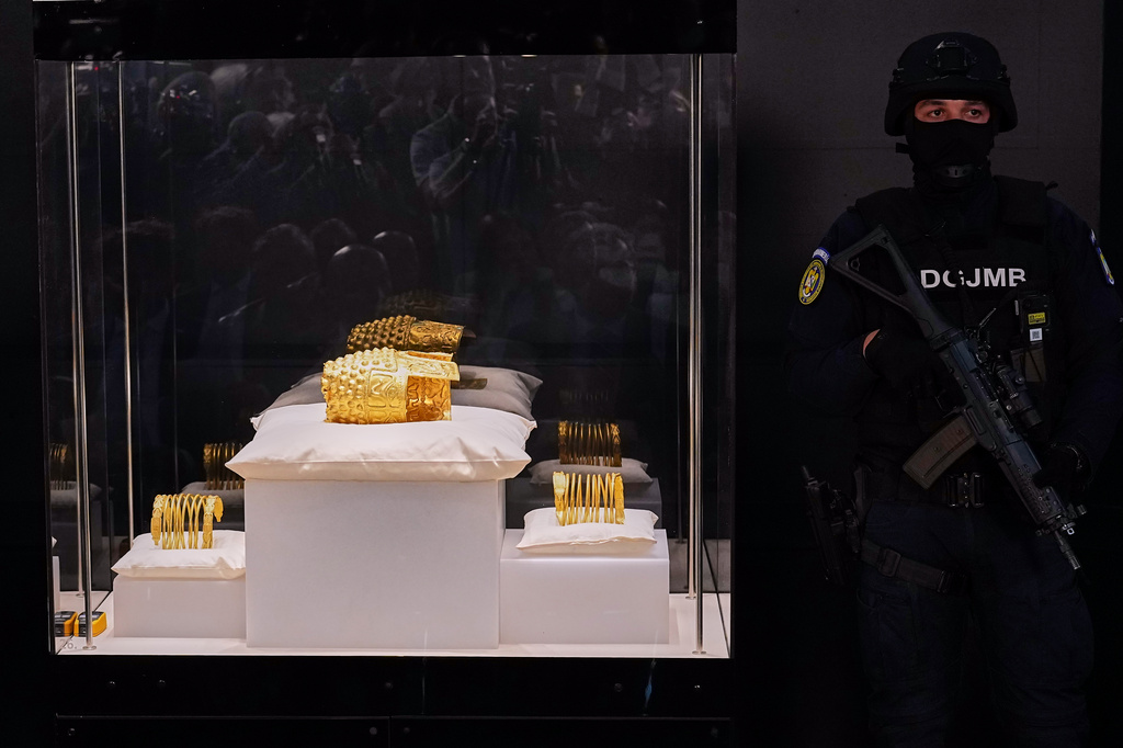 An armed gendarme stands by Dacian gold items, a 2,500-year-old helmet and wristbands, stolen from a museum in the Netherlands and then recovered by Dutch authorities, during a press conference after being returned, at the National Museum of Romanian History, in Bucharest, Romania, Tuesday, April 21, 2026. (AP Photo/Andreea Alexandru)