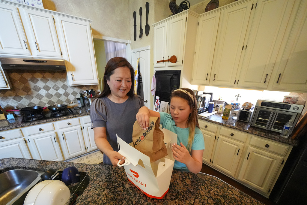 Janet Toth, left, and her daughter, Julep Toth, 9, open a delivery package after ordering a sandwich to their home Thursday, July 31, 2025, in Frisco, Texas. (AP Photo/Julio Cortez)