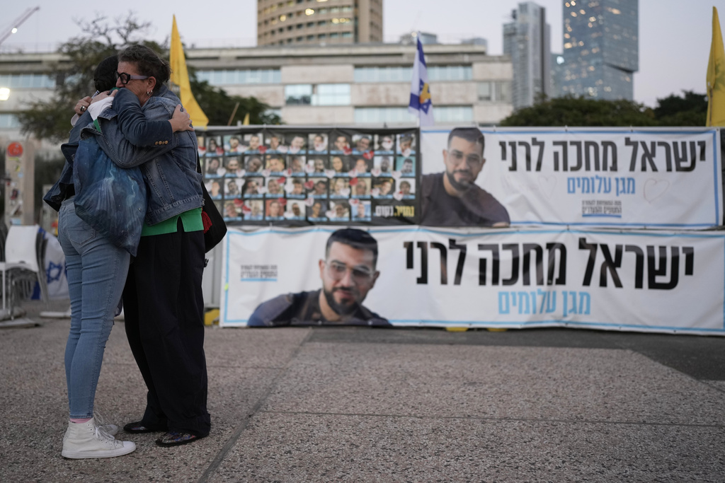 Two women embrace next to a banner with a photo of Ran Gvili after the announcement that the hostage, whose remains were the last to be recovered from Gaza, had been identified, in a plaza known as Hostages Square in Tel Aviv, Israel, Monday, Jan. 26, 2026. (AP Photo/Oded Balilty)