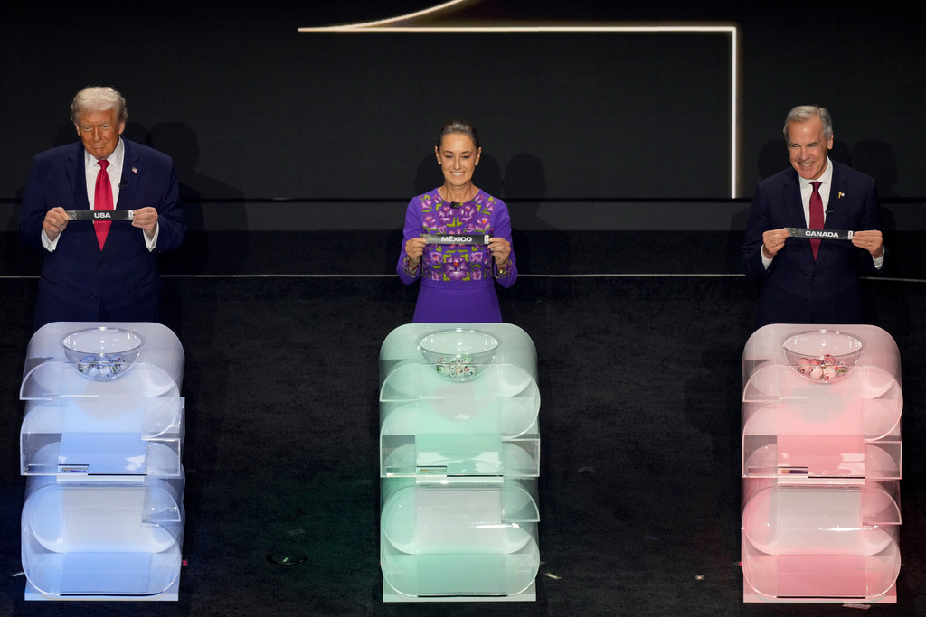 President Donald Trump, Mexican President Claudia Sheinbaum, and Canadian Prime Minister Mark Carney hold their host countries' names up during the draw for the 2026 soccer World Cup at the Kennedy Center in Washington, Friday, Dec. 5, 2025. (AP Photo/Alex Brandon)