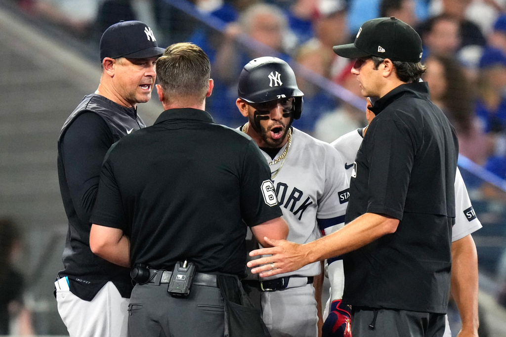 New York Yankees' José Caballero, third from left, and manager Aaron Boone, left, exchange views with home plate umpire Steven Jaschinski, second from left, and second base umpire John Tumpane, front right, during the sixth inning of a baseball game against the Toronto Blue Jays in Toronto, Sunday June 14, 2026. (Chris Young/The Canadian Press via AP)