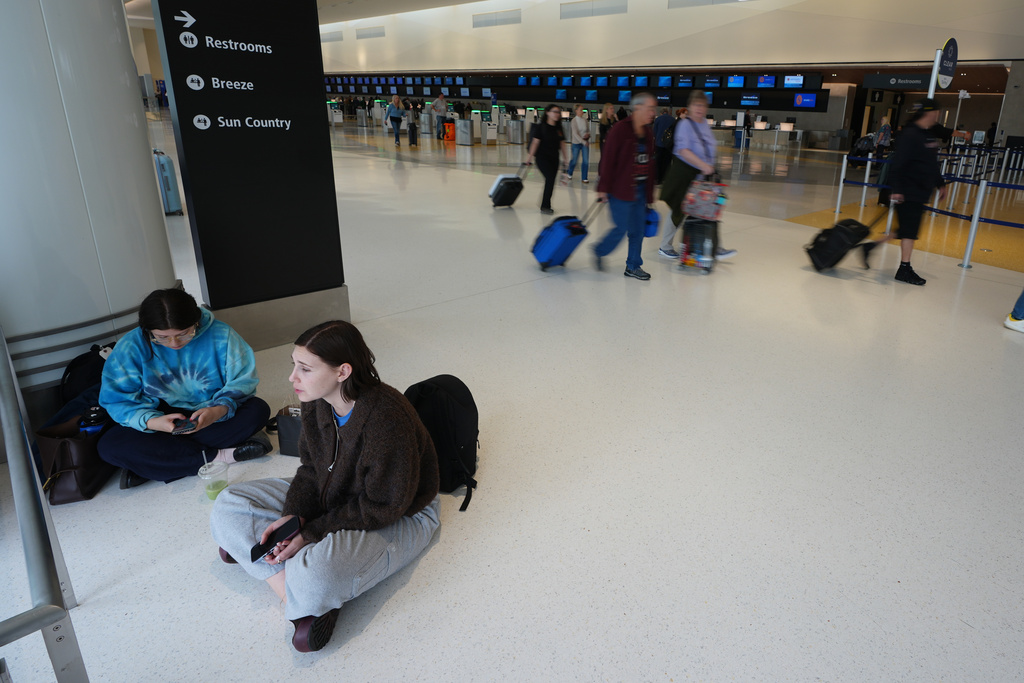 Grace Theodore, below center, and Isabel Azucena sit in a terminal at San Diego International Airport after learning their flight to New York was delayed by three hours Saturday, Nov. 8, 2025, in San Diego. (AP Photo/Gregory Bull)