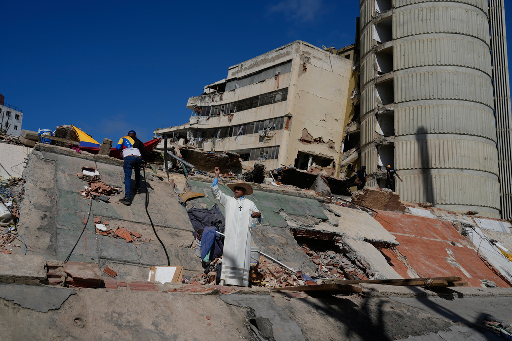 A Catholic priest stands in the rubble of residential buildings collapsed during the earthquakes that struck La Guaira, Venezuela, Friday, July 17, 2026. (AP Photo/Ariana Cubillos)