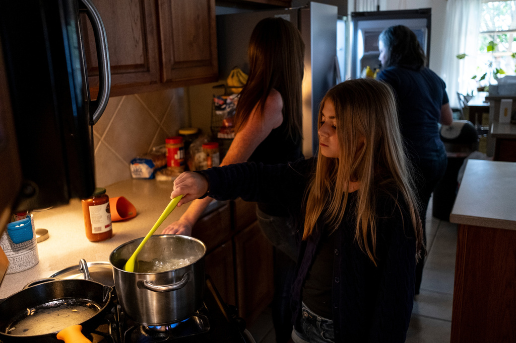 Ivy Edgar, 10, cooks pasta with her parents Jessica Edgar-Corum and Jamie Corum at their home on Monday, June 29, 2026, in Pflugerville, Texas. (AP Photo/Joel Angel Juarez)