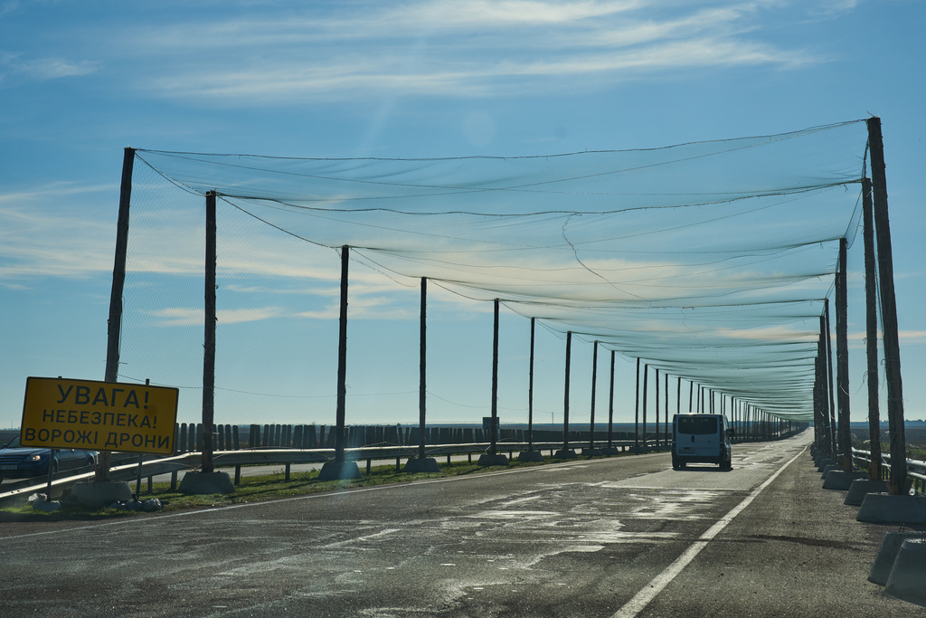A car drives on a road covered with an anti-FPV-drone net, a road sign reading "Attention/Danger/Enemy drones", at the approaches to the frontline city of Kherson, Southern Ukraine, Sunday, Nov. 2, 2025. (AP Photo/Efrem Lukatsky)