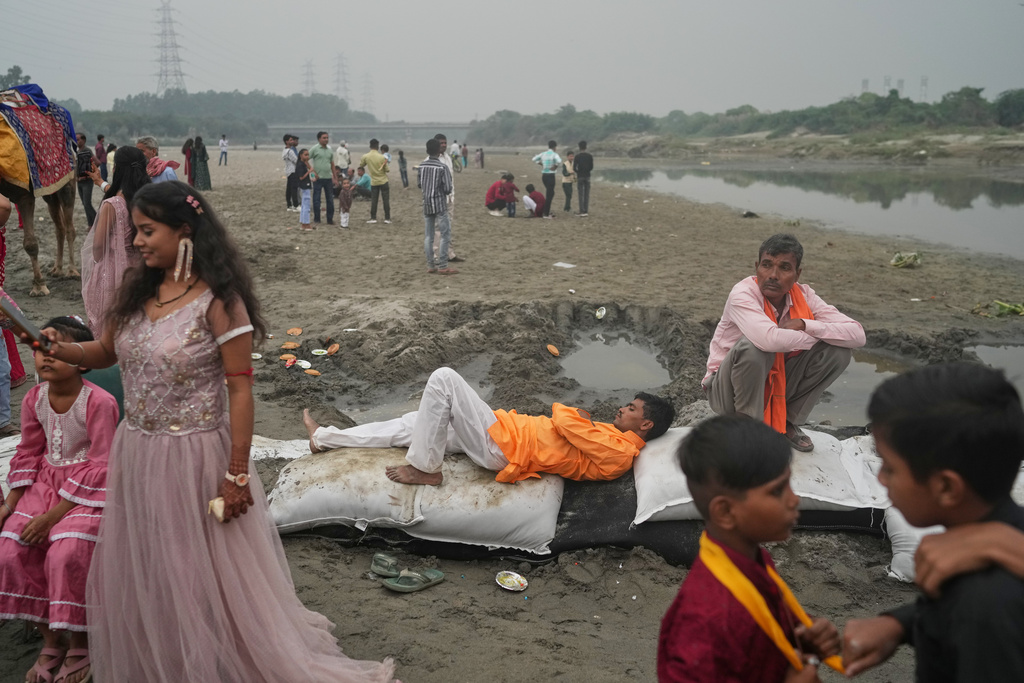 A person rests on the sand bags as devotees arrive on the banks of the river Yamuna during Chhath festival, which is celebrated for the well-being and prosperity of one's family, in New Delhi, India, Monday, Oct. 27, 2025. (AP Photo/Manish Swarup)