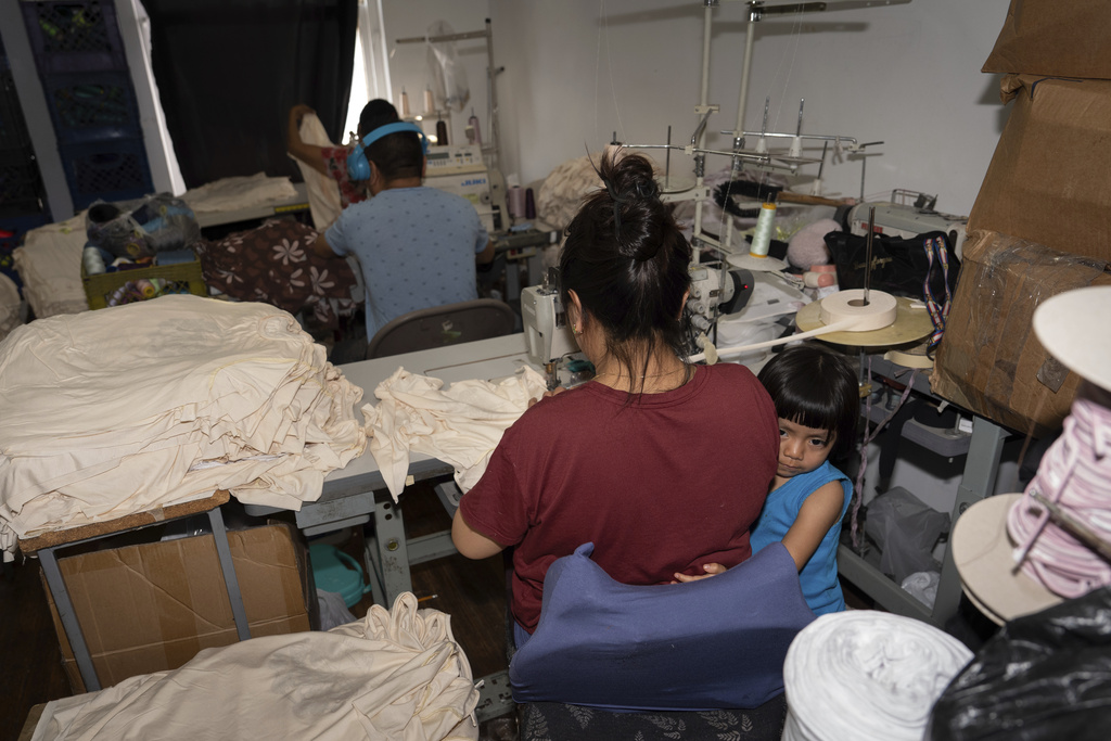 Anaise, de 3 anos, fica abraçada à mãe, Veronica, uma imigrante da Guatemala, enquanto ela trabalha em uma máquina de costura em Los Angeles, EUA, segunda-feira, 4 de agosto de 2025, em meio à onda de operações da polícia de imigração ICE. (Foto AP/Jae C. Hong)
