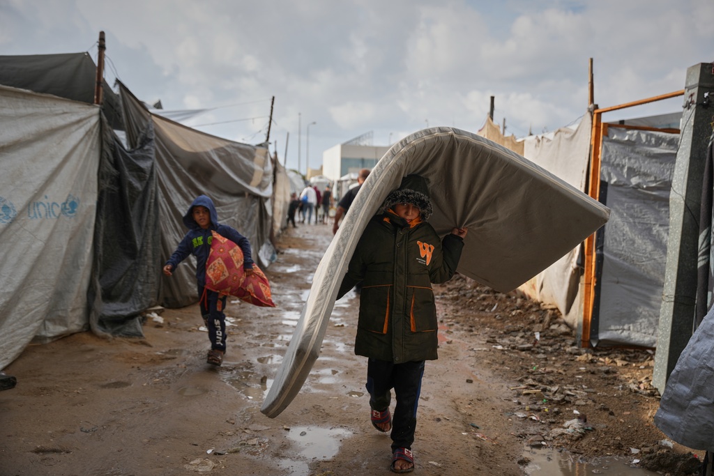 Salam Musa, 9, carries a mattress as he walks between tents after rainfall at a temporary camp in Deir al-Balah, in the central Gaza Strip, on Friday, Nov. 14, 2025. (AP Photo/Abdel Kareem Hana)