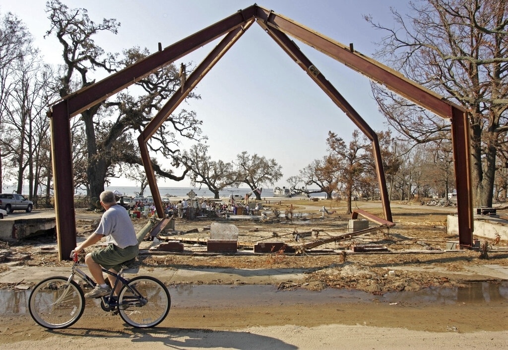 FILE - A cyclist rides by the remains of the Episcopal Church of the Redeemer while ministers conduct religious services on the beach in Gulfport, Miss., on Sept. 11, 2005. (AP Photo/Rob Carr, File)